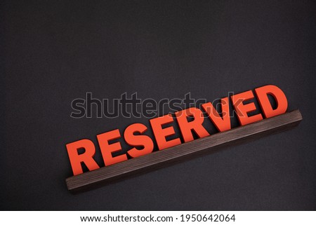 Service reserve at restaurant table. Large red plaque sign with wooden letters. Top view. Black background.