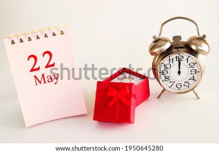 calendar date on light background with red gift box with ring and alarm clock with copy space. May 22 is the twenty-second day of the month.