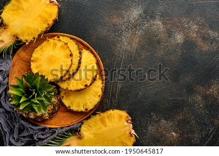 Sliced ripe pineapple on dark brown stone background. Tropical fruits. Top view. Free space for text. Mock up.