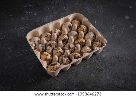 Small quail eggs in packaging on a dark background under concrete, close-up. High quality photo