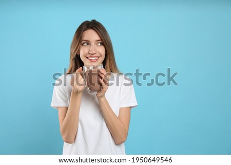 Young woman drinking chocolate milk on light blue background. Space for text