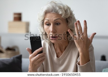 Angry shocked mature phone user staring at screen in surprise. Elderly lady worried about app error, data stealing, scam, bad news, problems with smartphone. Annoyed woman using cell for video call Royalty-Free Stock Photo #1950650455