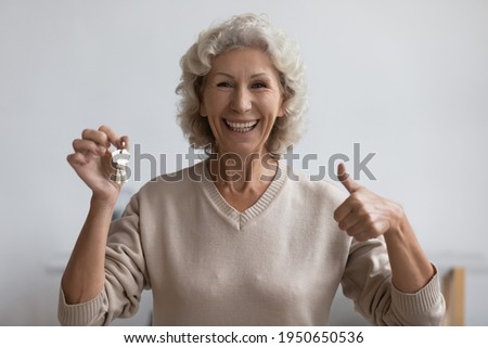 Excited elderly lady getting key from new home, showing like thumb up gesture at camera. Happy senior woman buying renting house. Real estate, property purchase, mortgage concept. Head shot portrait