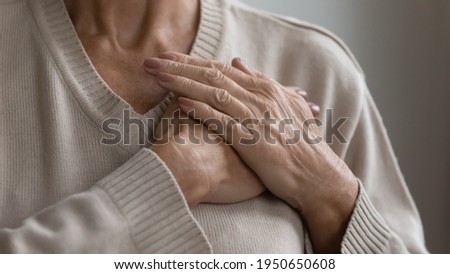 Mature elderly woman feeling heart pain, touching chest with both hands. Thankful senior lady expressing gratitude, love, trust, thanking god, making grateful honor kindness gesture. Close up Royalty-Free Stock Photo #1950650608
