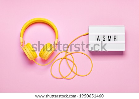 Yellow headphones and ASMR letters lightbox on pink background. ASMR Stress-relieving sounds concept, flat lay
