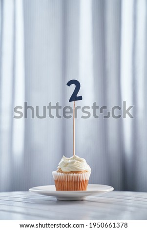 Minimalistic birthday or anniversary concept. Homemade vanilla birthday cupcake with creamy topping and number 2 two on white plate and bright background. High quality vertical image