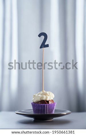 Tasty chocolate homemade cupcake or muffin with number 2 on black plate and bright background. Minimalistic anniversary or birthday concept. High quality vertical photo