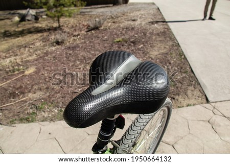 A foam cushioning bicycle saddle, or seat, without center cut out shot from a side angled view  on a driveway in Ontario, Canada. Rider standing behind in the distance, wheel and spokes visible. 
