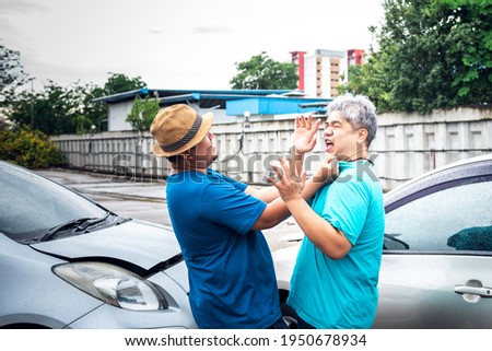 Two Asian middle-aged fat man are arguing, due to a accident car crash, while it was raining, to people and accident insurance concept. Royalty-Free Stock Photo #1950678934