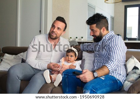 gay couple and their daughter sitting on the sofa watching television. The girl watches the cartoons attentively