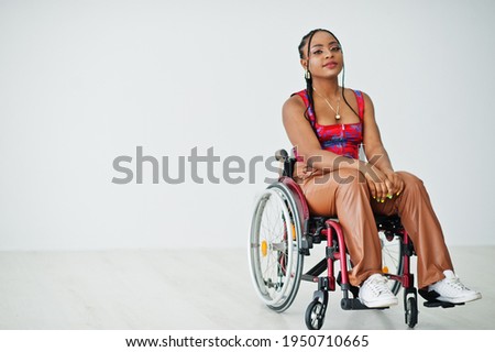 Young disabled African American woman in wheelchair against white wall. Royalty-Free Stock Photo #1950710665
