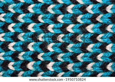 Synthetic knitted fabric with pattern elements of blue, black and white yarns close up. Multicolor patterned knitted fabric texture. Background