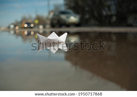 Spring in the city paper boat in a puddle. A snow-white boat made from a drawing of documents floats along spring street in a stream of meltwater.