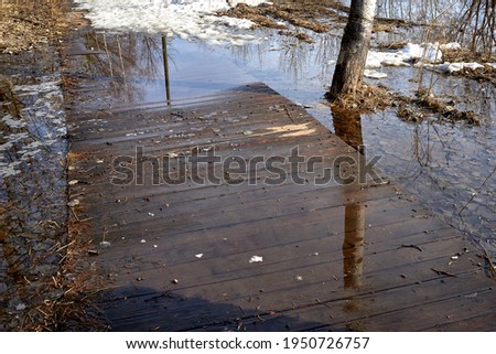 The wooden bridge in the park is flooded with water from the melting snow. Spring landscape.