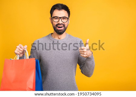 It's shopping time! Happy bearded happy young man with colorful paper bags isolated over yellow background.