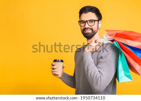 It's shopping time! Happy bearded happy young man with colorful paper bags isolated over yellow background.