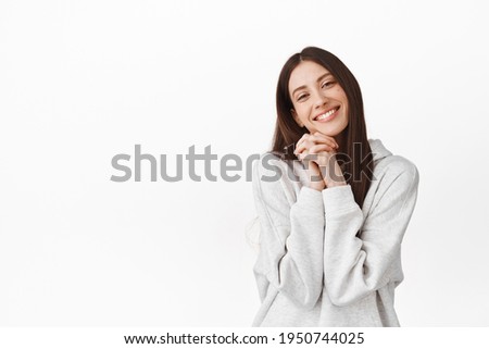 So adorable. Cute beautiful girl fascinated by something, holding hands near face and smiling, looking at lovely tender scene, watching romantic moment, standing over white background