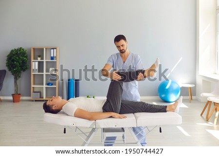 Man professional doctor osteopath in uniform moving up and checking man patients legs joints Royalty-Free Stock Photo #1950744427