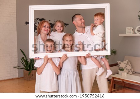 large family, parents and four children holding picture frame look into the camera