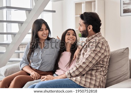 Happy indian family couple with teen child daughter bonding, hugging, talking sitting on couch at home. Smiling husband and wife embracing child spending time together relaxing on sofa in living room Royalty-Free Stock Photo #1950752818