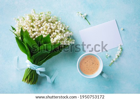 Coffee cup with spring bouquet of flowers lily of the valley and empty greeting card top view. Good morning breakfast concept.
