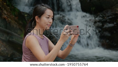 Woman use cellphone to take photo at waterfall in rain forest