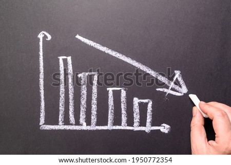 Hand sketching decreasing graph on chalkboard, business going down, decrease sales and revenue in economic crisis Royalty-Free Stock Photo #1950772354