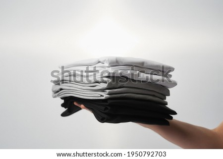 Basic outfit. Male hand holding stack of multi colored t-shirts against grey background. Casual clothes for men and women, fashion and style concept Royalty-Free Stock Photo #1950792703