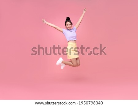 Happy Asian woman smiling and jumping while celebrating success isolated over pink background. Royalty-Free Stock Photo #1950798340