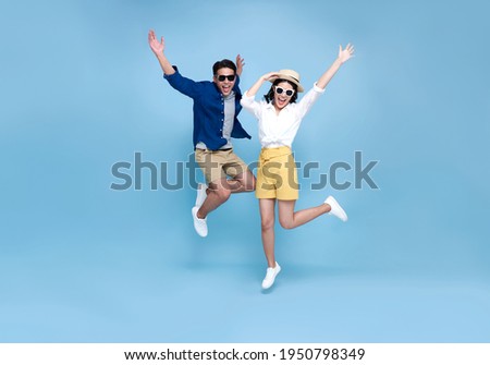 Happy Asian couple tourist jumping celebrating to travel on summer holiday isolated on blue background.