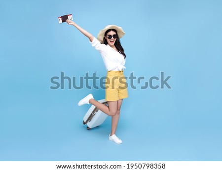 Happy smiling Asian woman dressed in summer clothes with passport and luggage enjoying their summer vacation getaway in blue background. Royalty-Free Stock Photo #1950798358