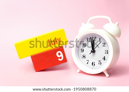 July 9th. Day 9 of month, Calendar date. White alarm clock on pastel pink background. Summer month, day of the year concept