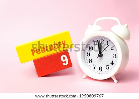 February 9th. Day 9 of month, Calendar date. White alarm clock on pastel pink background. Winter month, day of the year concept