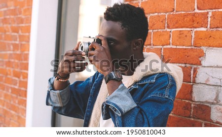 Portrait close up of stylish photographer african american man with film camera taking a picture on a city street