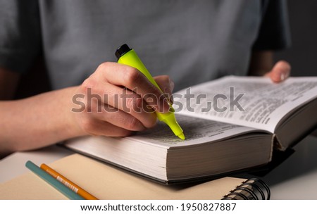 Female student hands holding yellow highlighter and reading book or textbook, underlines, prepare for exam at table at night. Education concept. Royalty-Free Stock Photo #1950827887