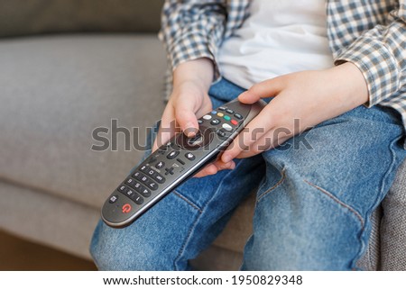 Close-up kid hands holding TV remote controller. Boy without parental control watching television. Early childhood education and elementary age leisure.