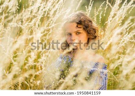 A girl laughs in a field, among the grass with a bouquet of wildflowers