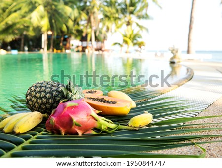 tropical fruits on a background of palm leaves by the pool