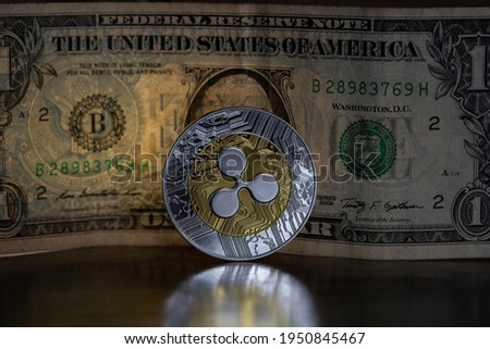 Ripple XRP cryptocurrency physical coin placed next to US dollar in the dark background