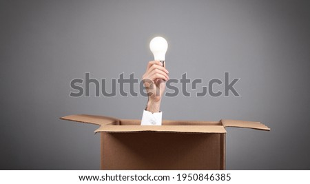 Male hand holding a light bulb coming out from a cardboard box.
