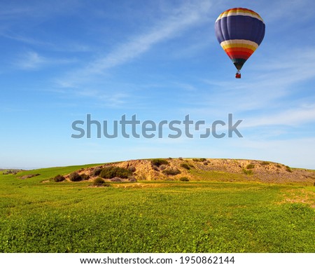 The bright multicolor hot air balloons flies over the field. Beautiful sunny day in April. Spring bloom of the Negev Desert in Israel. Fields of spring grass in the bright southern sun.