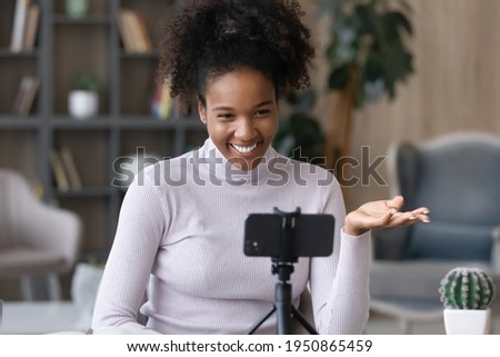 Smiling young African American woman use modern smartphone talk speak on video call on gadget. Happy millennial biracial female look at cellphone camera have webcam online lesson or virtual event. Royalty-Free Stock Photo #1950865459