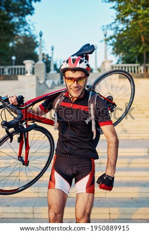 Young and energetic cyclist in the park. Man climbs the stairs holding a bike on his shoulder