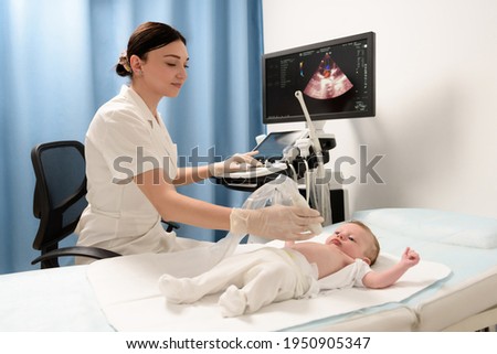 A female doctor conducts an ultrasound examination of the heart and abdominal organs of a newborn boy using modern medical equipment in a clinic. Pediatrics and child development monitoring Royalty-Free Stock Photo #1950905347