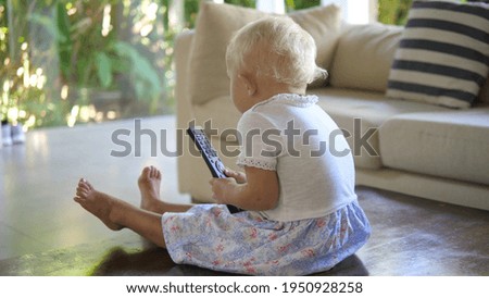 Digital parenting concept. Abandoned blonde baby girl playing alone with the remote control