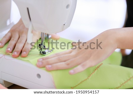 Selective focus on hand. Woman seamstress sitting and sews. Lady makes stitch and repair broken clothes by skill on sewing machine. Concept dressmaker service for customer