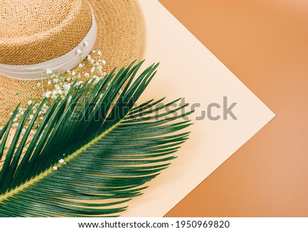 Tropic leaves, straw hat on brown background. Trendy fashion accessories. Flat lay, close up. Summer, vacation, holidays concept.