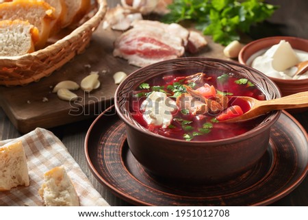 Freshly cooked hot homemade borscht - traditional dish of Russian and Ukrainian cuisine in earthenware dishes with bacon, bread, sour cream and garlic