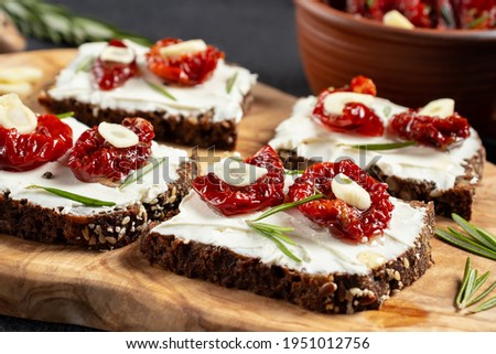 Homemade multigrain bread sandwiches with cream cheese and sun-dried tomatoes on a wooden platter, close-up. Healthy eating concept