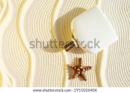 white perfume bottle on a sandy textured background with seafish. Summer scent concept for vacation Royalty-Free Stock Photo #1951026406